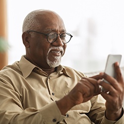Man with glasses smiling while looking at phone