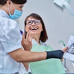 Woman smiling with dentist while reviewing X-ray